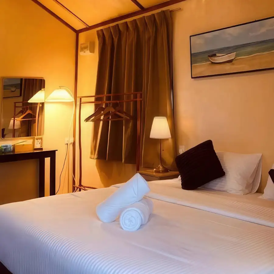 A cozy bedroom at Coco Seaweed Resort near Semporna showing a comfortable bed, warm lighting, a vaulted wooden ceiling, clothes rack, authentic glossy hardwood floors, and air conditioning.